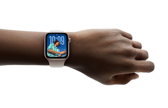 Close-up of Apple Watch in Silver with rubber strap on a person’s wrist, showing Time app in new Liquid Glass design