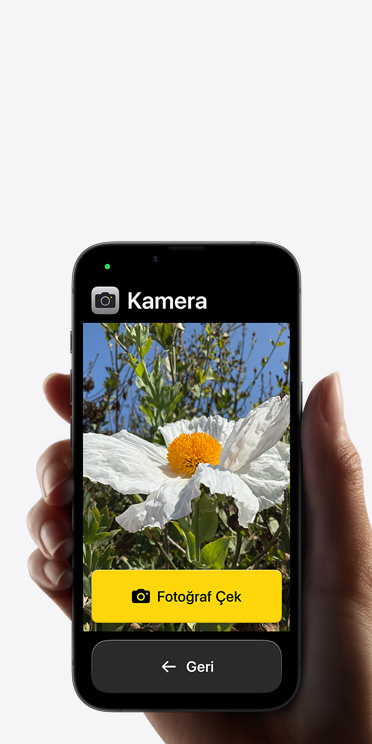 Kadrajında beyaz çiçek bulunan Kamera uygulamasının basitleştirilmiş arayüzünü, “Fotoğraf Çek” düğmesini ve altındaki “Geri” düğmesini gösteren iPhone 16e ekranı