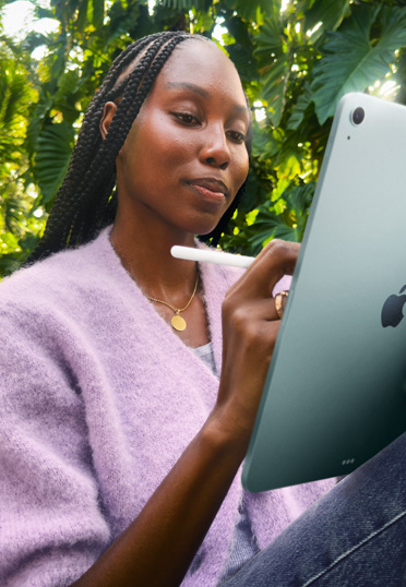 一名學生坐在戶外，她手拿著一台 iPad 和一支 Apple Pencil Pro。