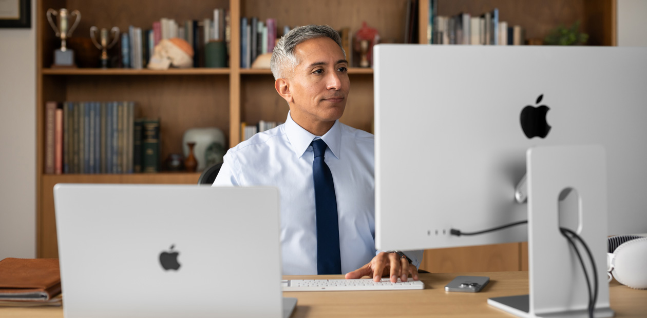 A provider sitting at his desk while looking at an iMac and MacBook Pro.