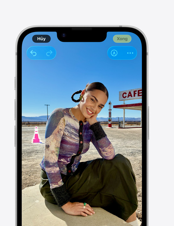 Màn hình iPhone, ảnh chụp một người đang mỉm cười trên bãi biển, thể hiện cách xóa cọc tiêu hình nón trong hậu cảnh bằng công cụ Dọn Dẹp